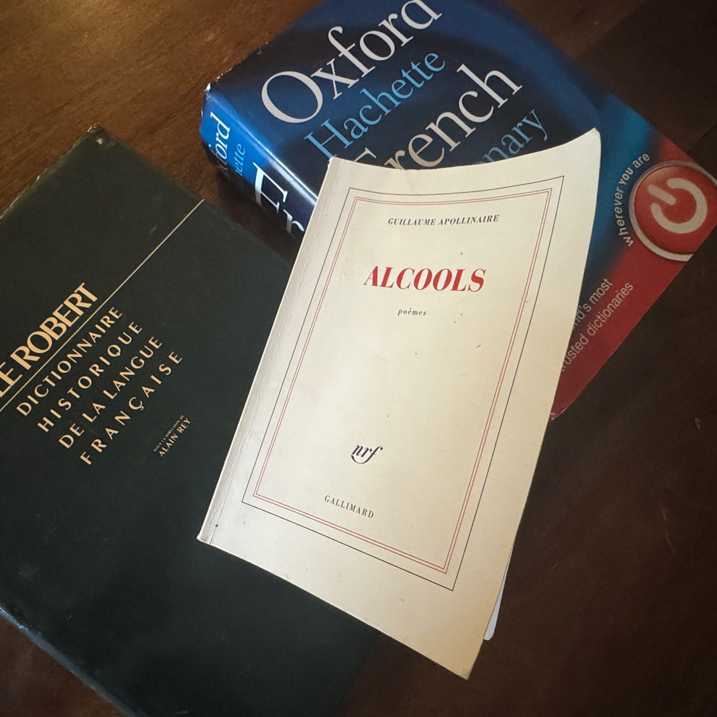 A copy of Gallimard's edition of Guillaume Apollinaire's Alcools, on top of a French-English dictionary and a historical dictionary of French