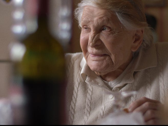 A photo of Lucy in her elder years, wearing a white sweater and looking to her right. She is smiling at something off camera. 