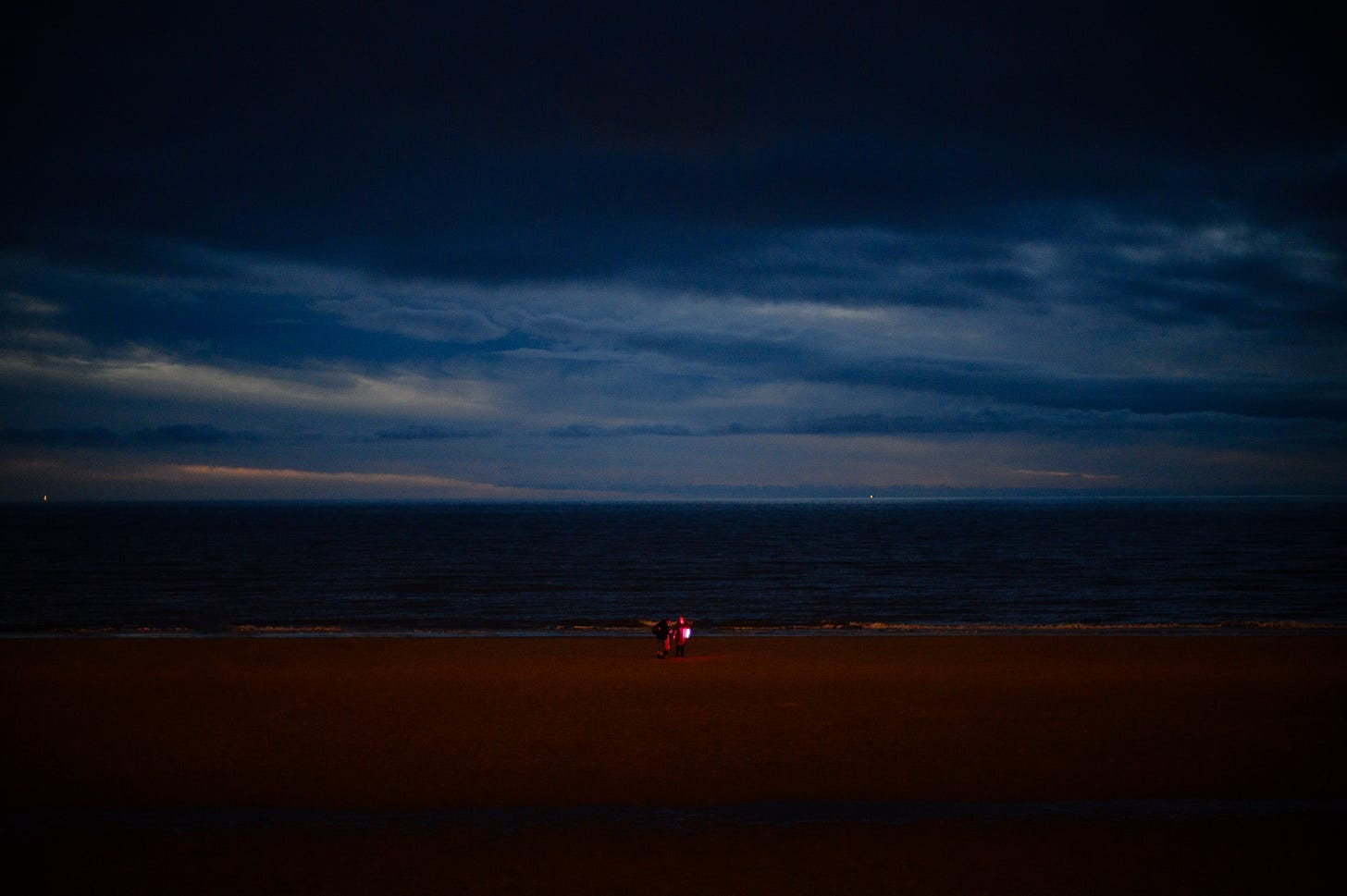 A group of people play with a purple light on the beach at dusk.