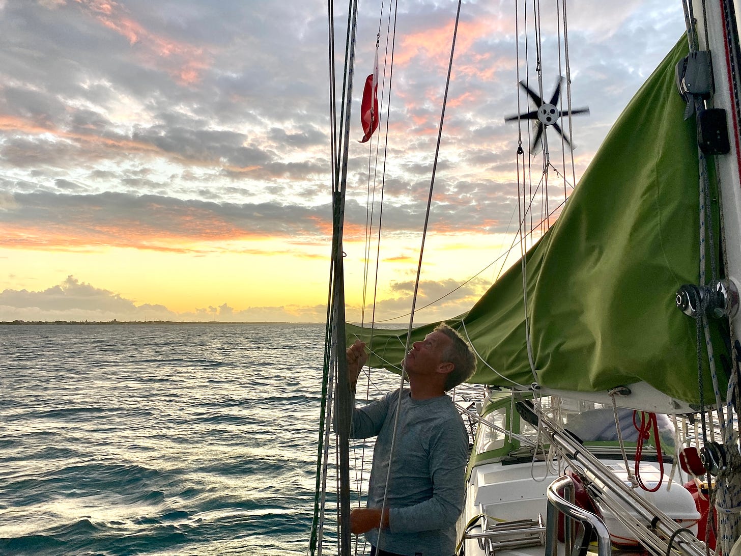 A beautiful sunset as seen from the deck of a sailboat as a man raises the Tongan flag