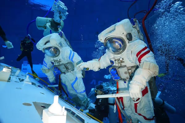 Two taikonauts training for an extravehicular activity in a neutral bouncy pool.