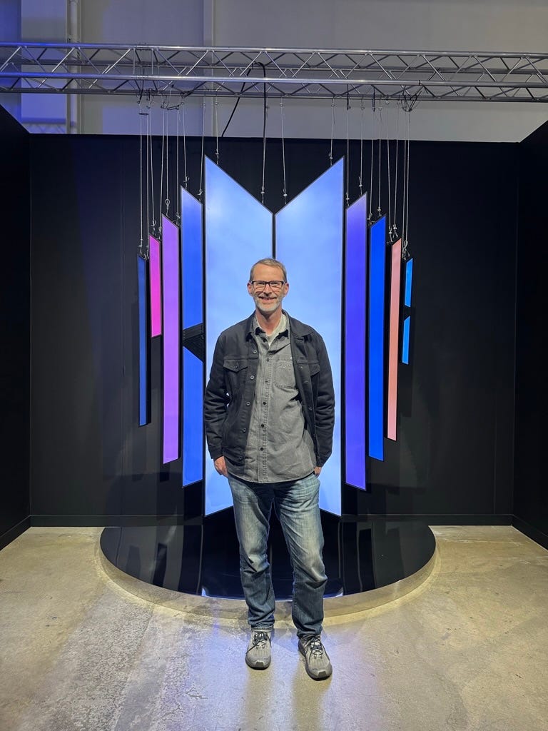 Tom Merrit stands in front of neon BTS logo