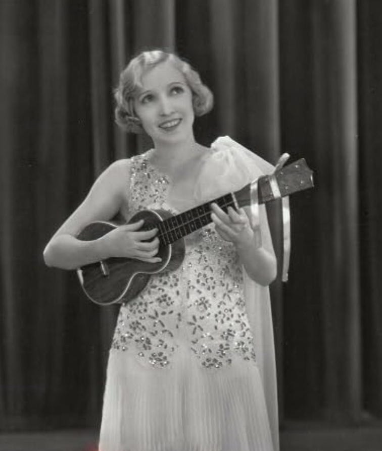 Bessie Love, smiling and playing a ukulele