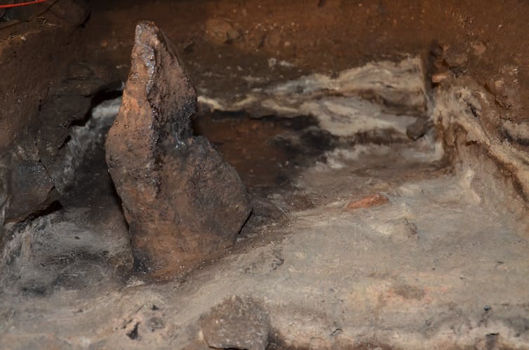 A small elongated stone standing upright in ashy sediments.