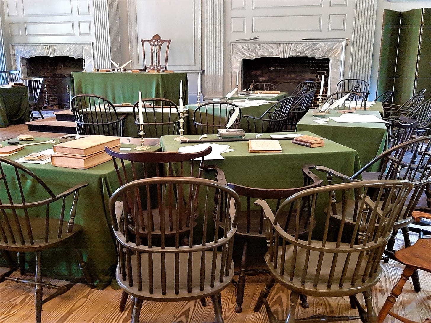 Old wooden chairs around tables with green cloths where the founders created the declaration of independence.