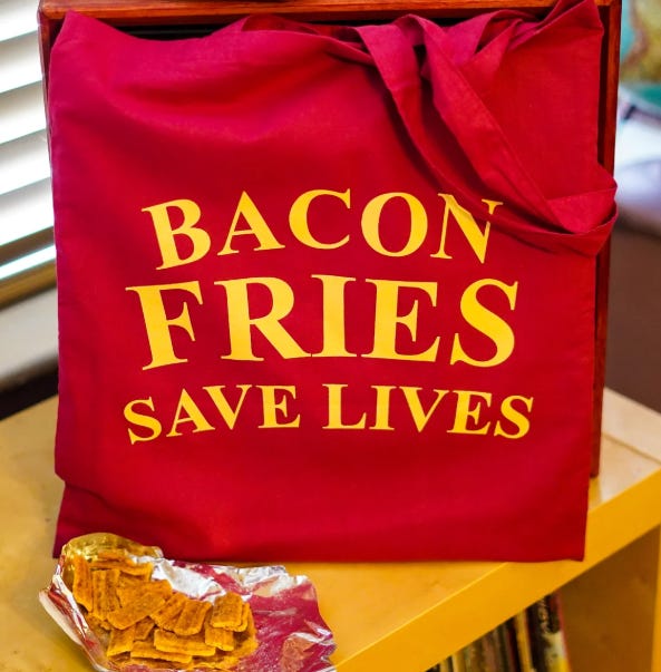 A red tote bag with "Bacon Fries Save Lives" in yellow printed on it