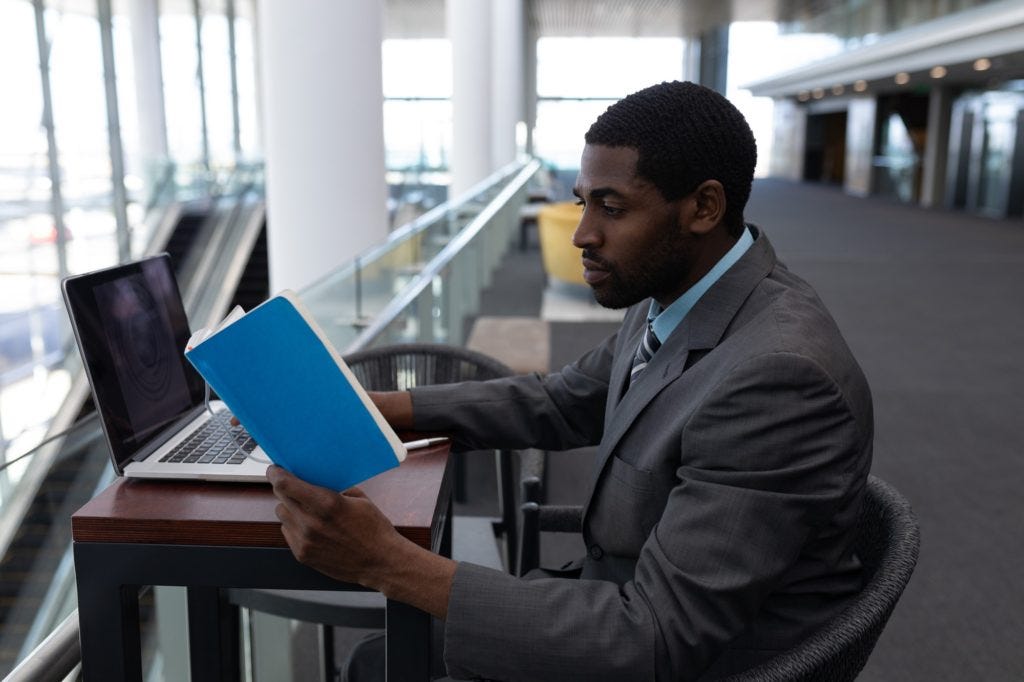 Businessman with laptop sitting at table and reading a book in modern office