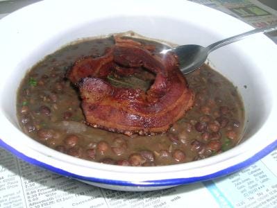 An enamel bowl full of slow cooked Carlin peas with bacon on top