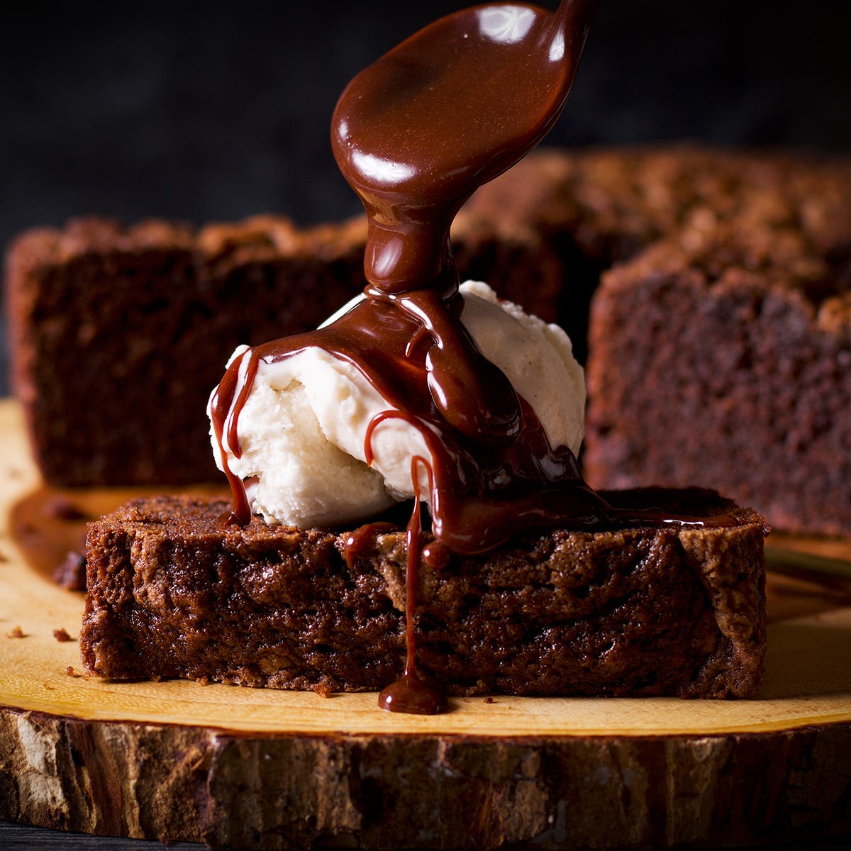 Drizzling hot fudge over a slice of chocolate loaf cake and a scoop of vanilla ice cream.