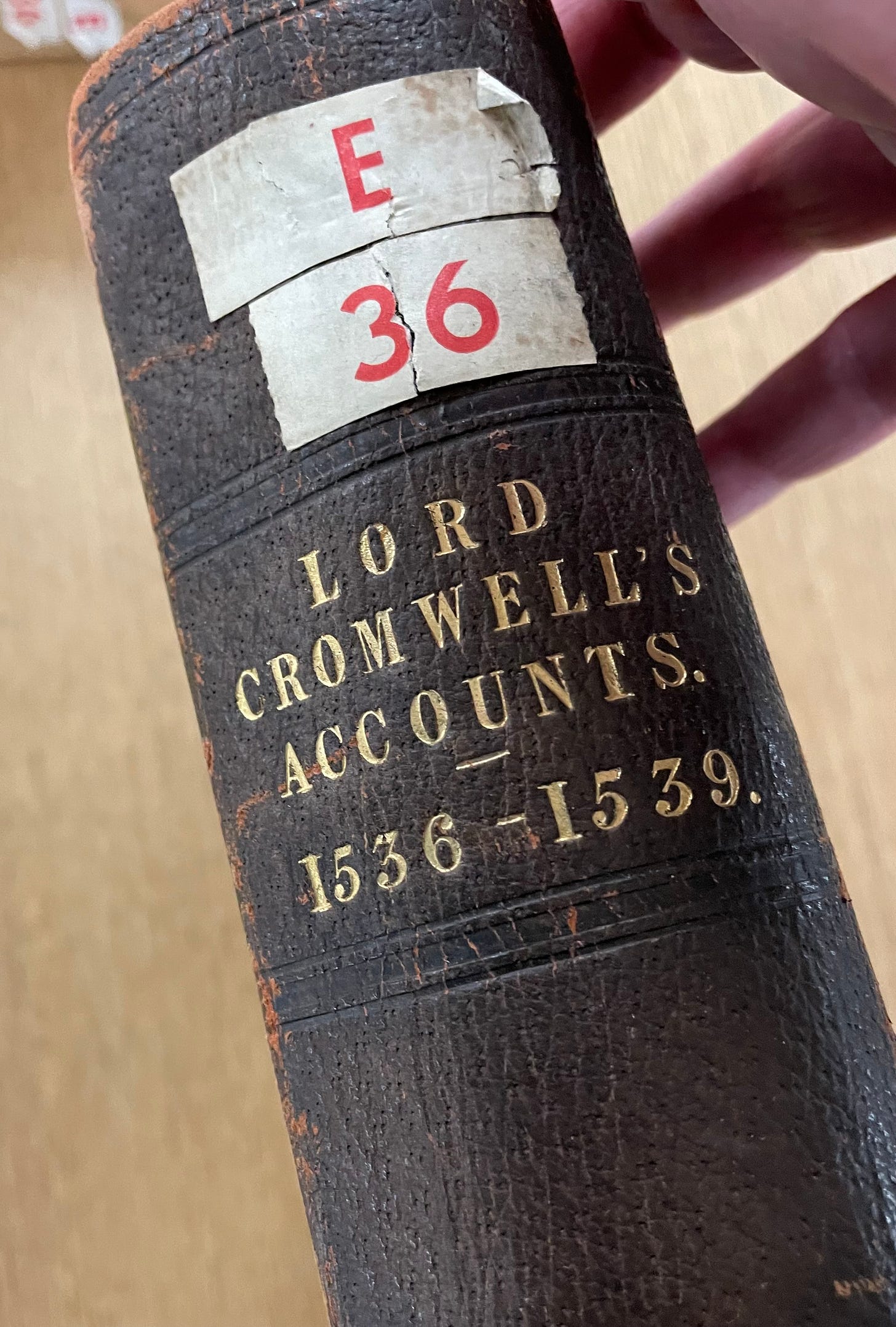 A hand holds a large leather bound book, with Lord Cromwell’s Accounts 1536-1539 tooled in gold on the spine
