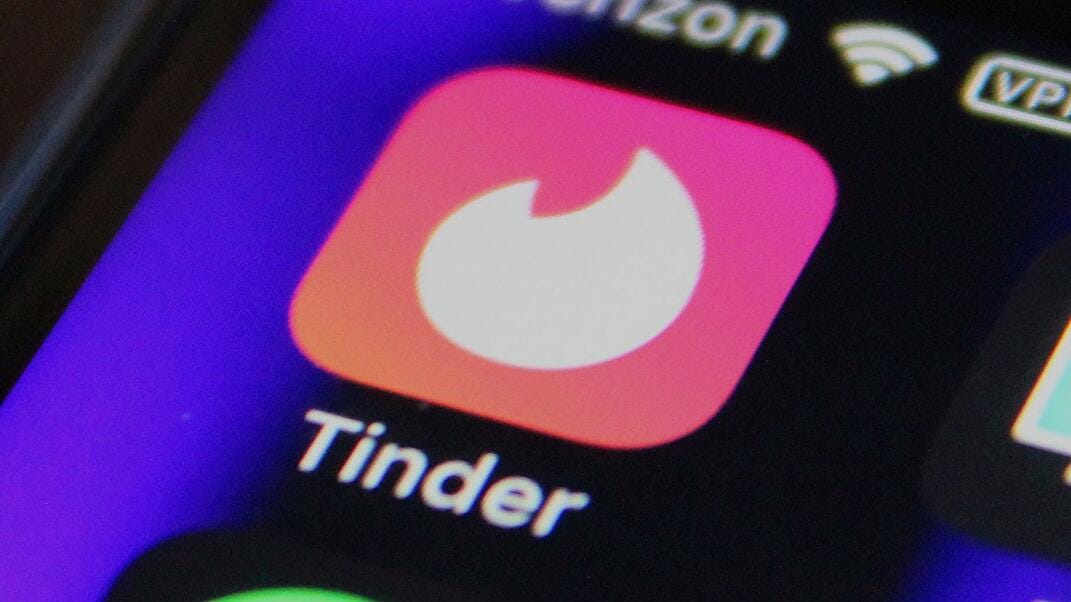 An image of a telephone screen with the Tinder app logo on it – a white flame on a pink square background