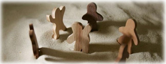 Plain wooden people figures stand in some sand