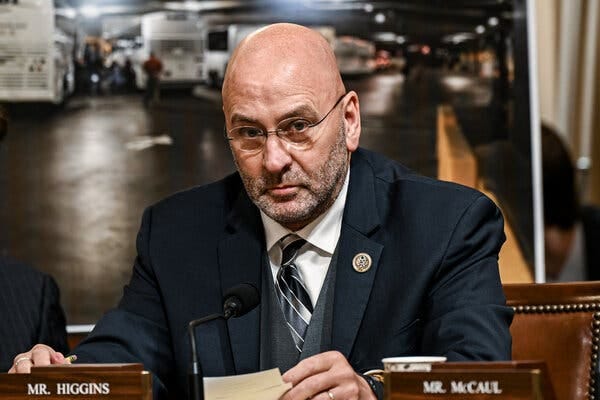 Representative Clay Higgins, Republican of Louisiana, sits in a chair as he holds papers during a House hearing. In front of him are a microphone and a nameplate reading “Mr. Higgins.”