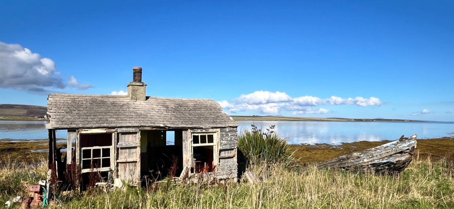 Image of an dilapidated shed & boat with the sea behine. the sun & sea are blue 