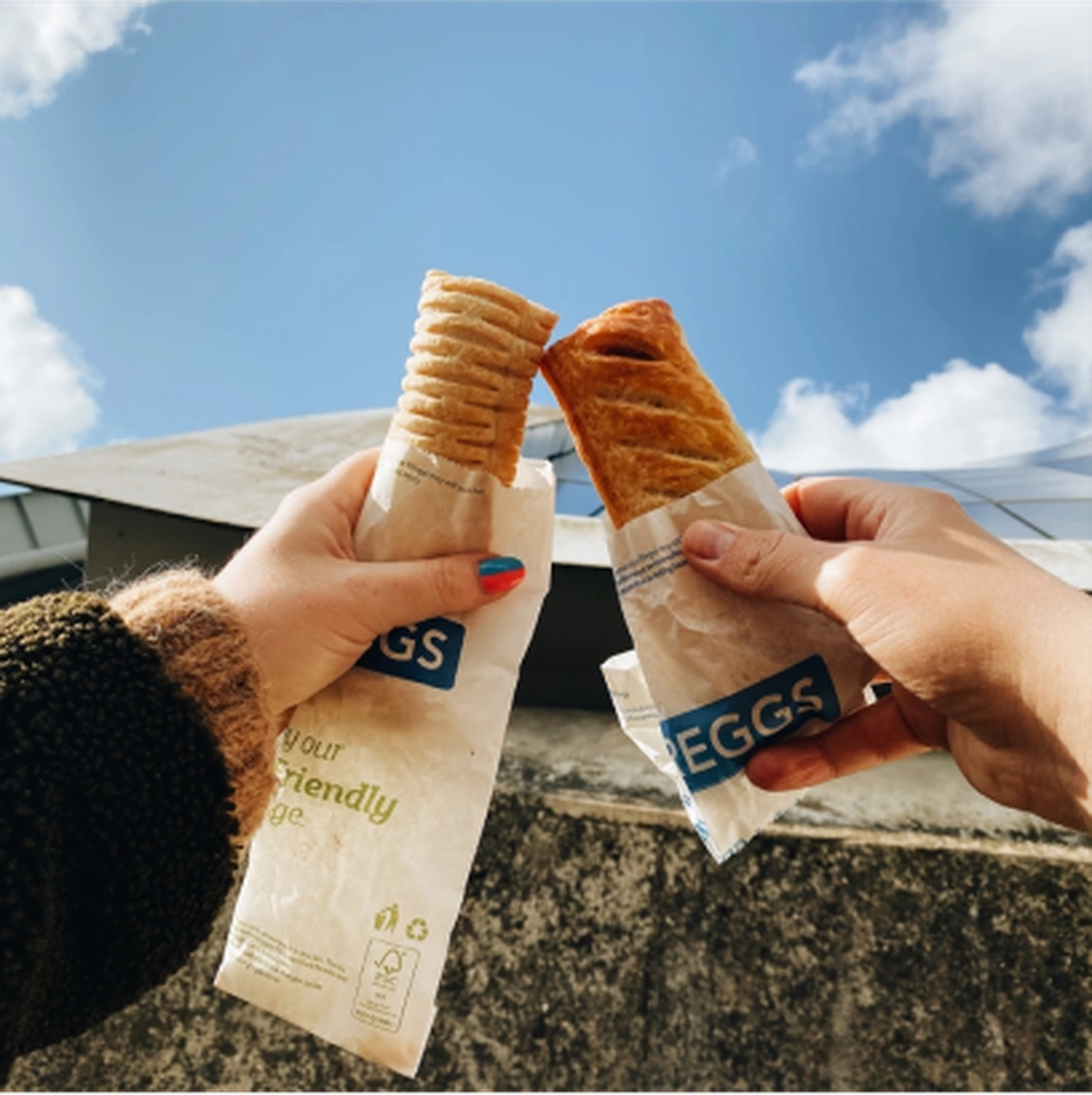 Two people holding a sausage roll and a vegan sausage roll
