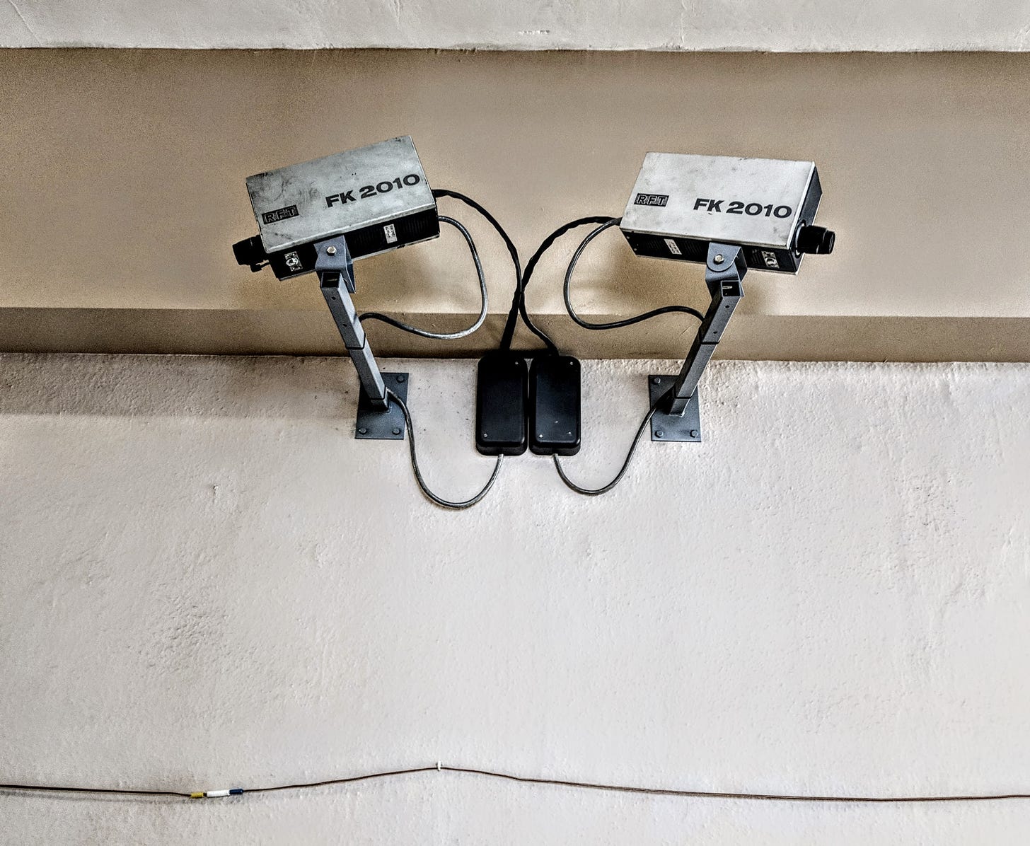 Two outdated security cameras point in opposite directions down a hallway. Text printed on the side of each says "FK 2010."