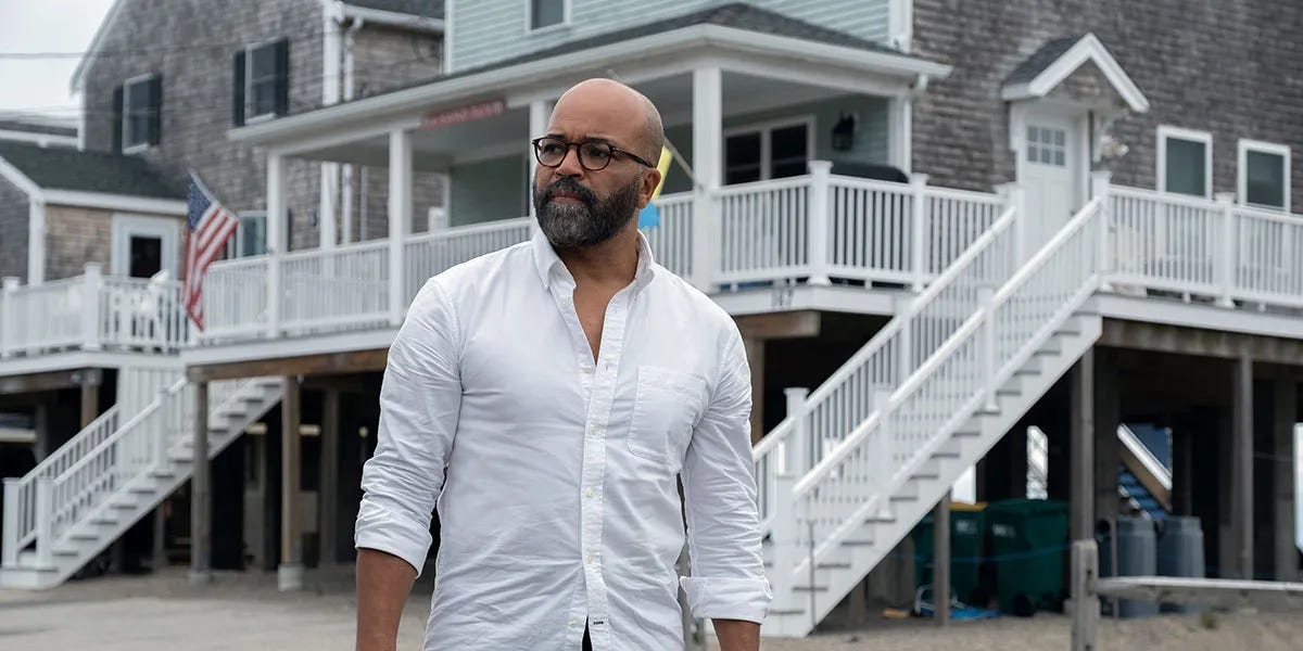 Black man with glasses wearing a white button down in front a grey beach house