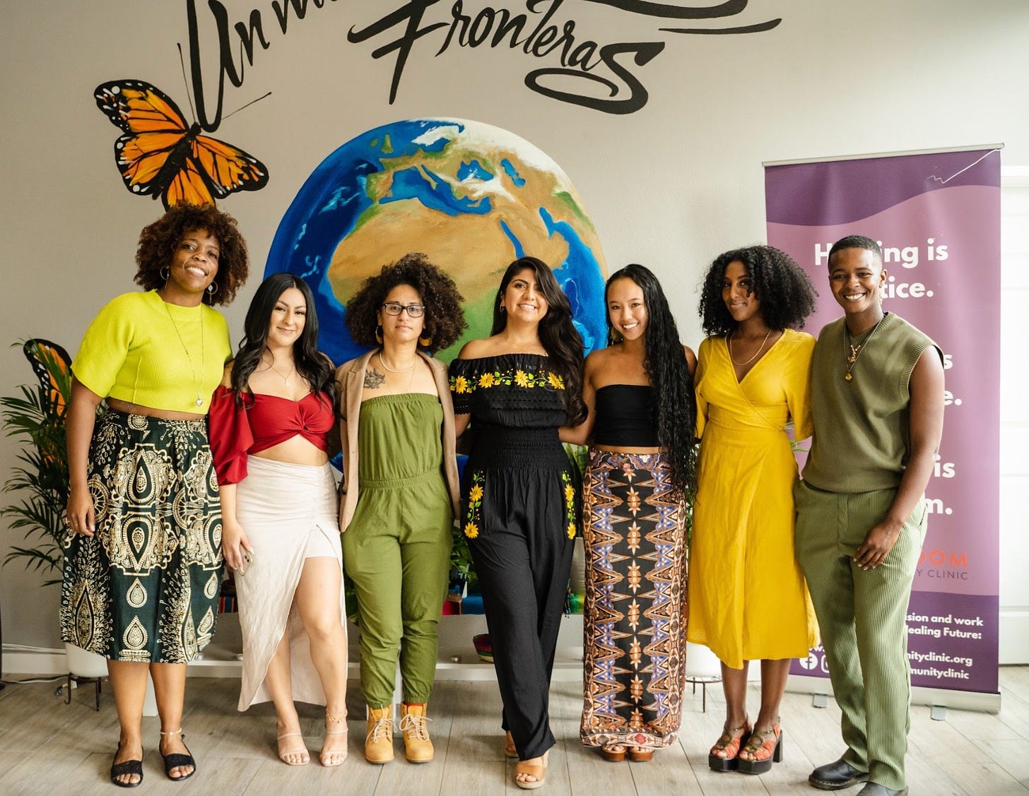 Bernie and the other members of the core organizing team stand in front of a moral at their Community Healing Sanctuary. It reads Un mundo sin fronteras."