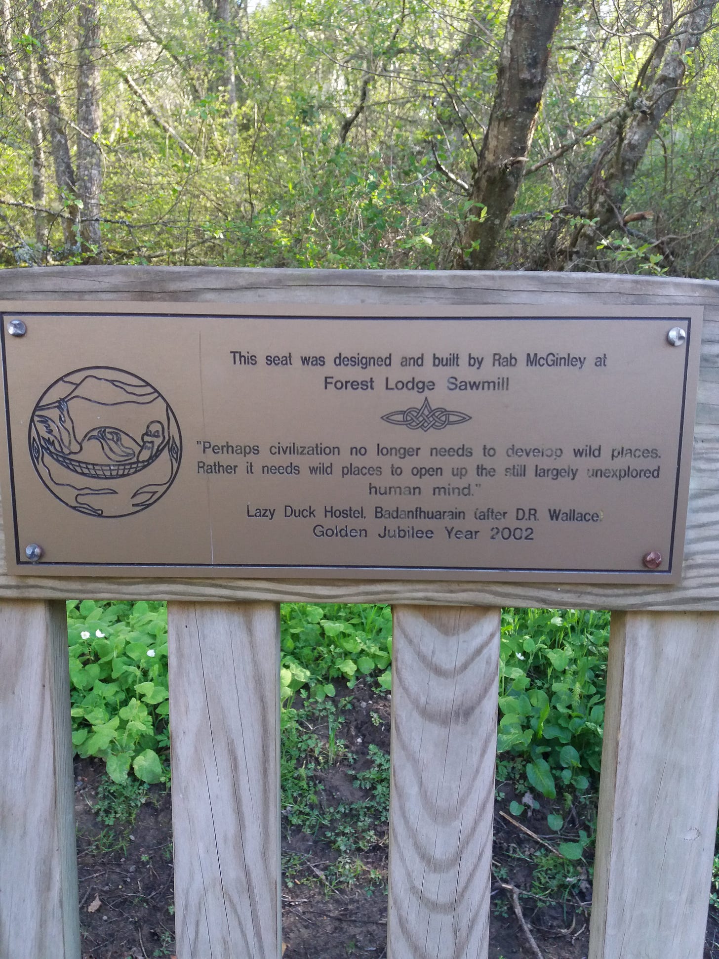 Brass plaque on wooden bench reading "Perhaps civilisation no longer needs to develop wild places. Rather it needs wild places to open up the still largely unexplored human mind."