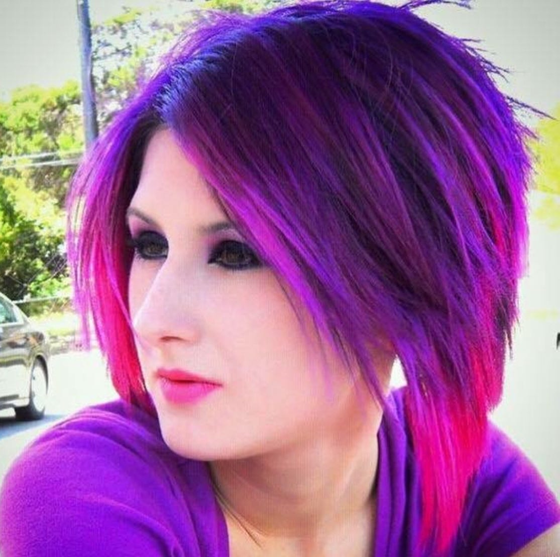 Old photo of Lyric, in their mid-20s, with hot pink and purple hair, matching lipstick, makeup, and shirt. 