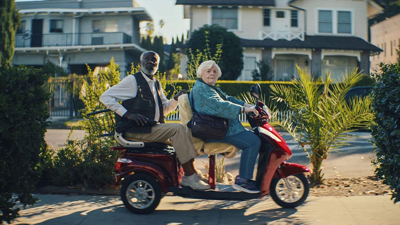 A screenshot from the movie Thelma showing two senior citizens on a motorized scooter.