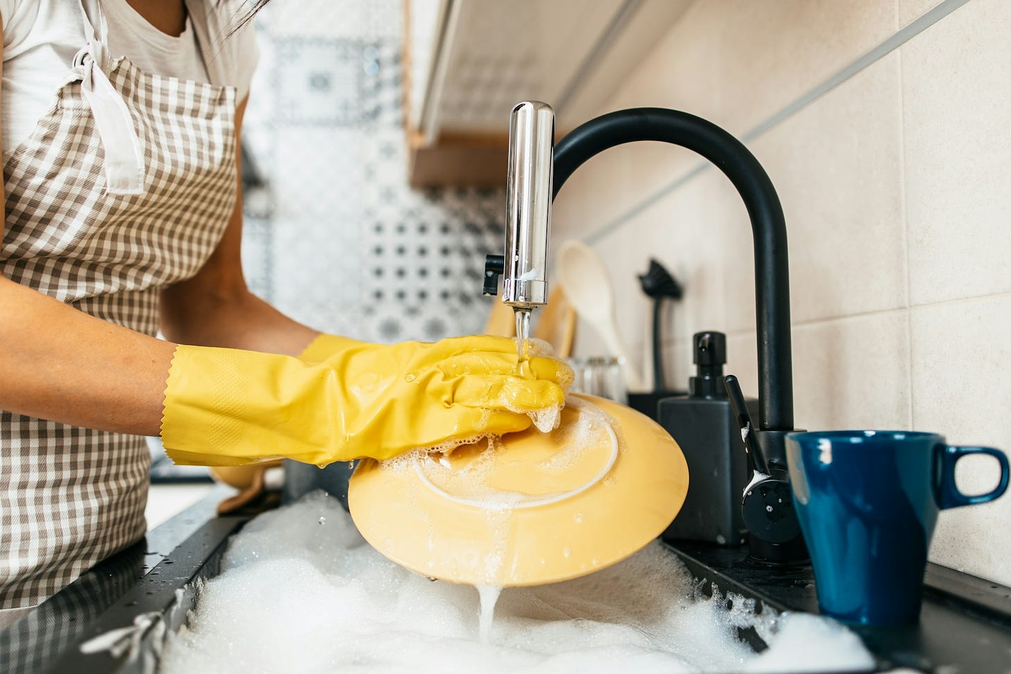 A woman with yellow gloves on washing a yellow dish in her sink.
