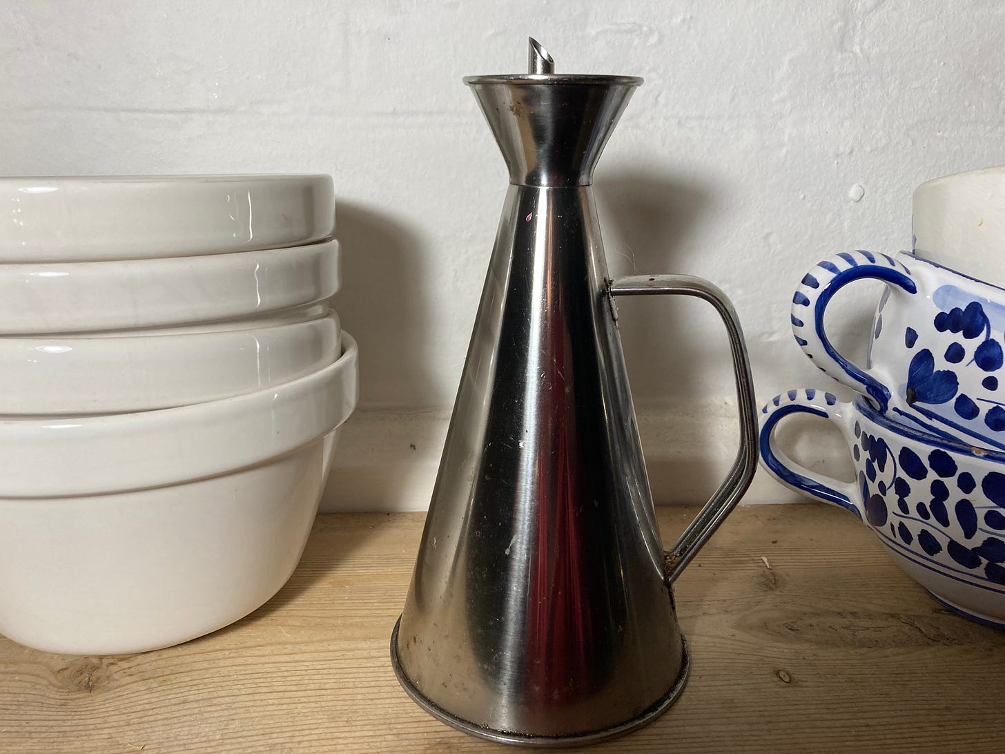 Stainless steel oil drizzler on a shelf with Mason Cash bowls and Deruta cups