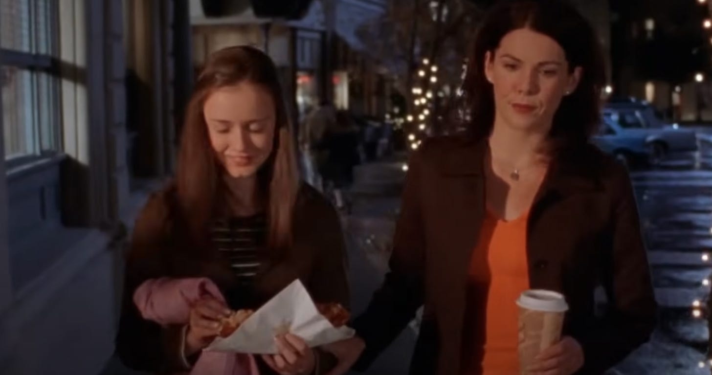 Rory on the left is holding a pizza crust, and Lorelai on the righ is holding a takeout cup of coffee. 