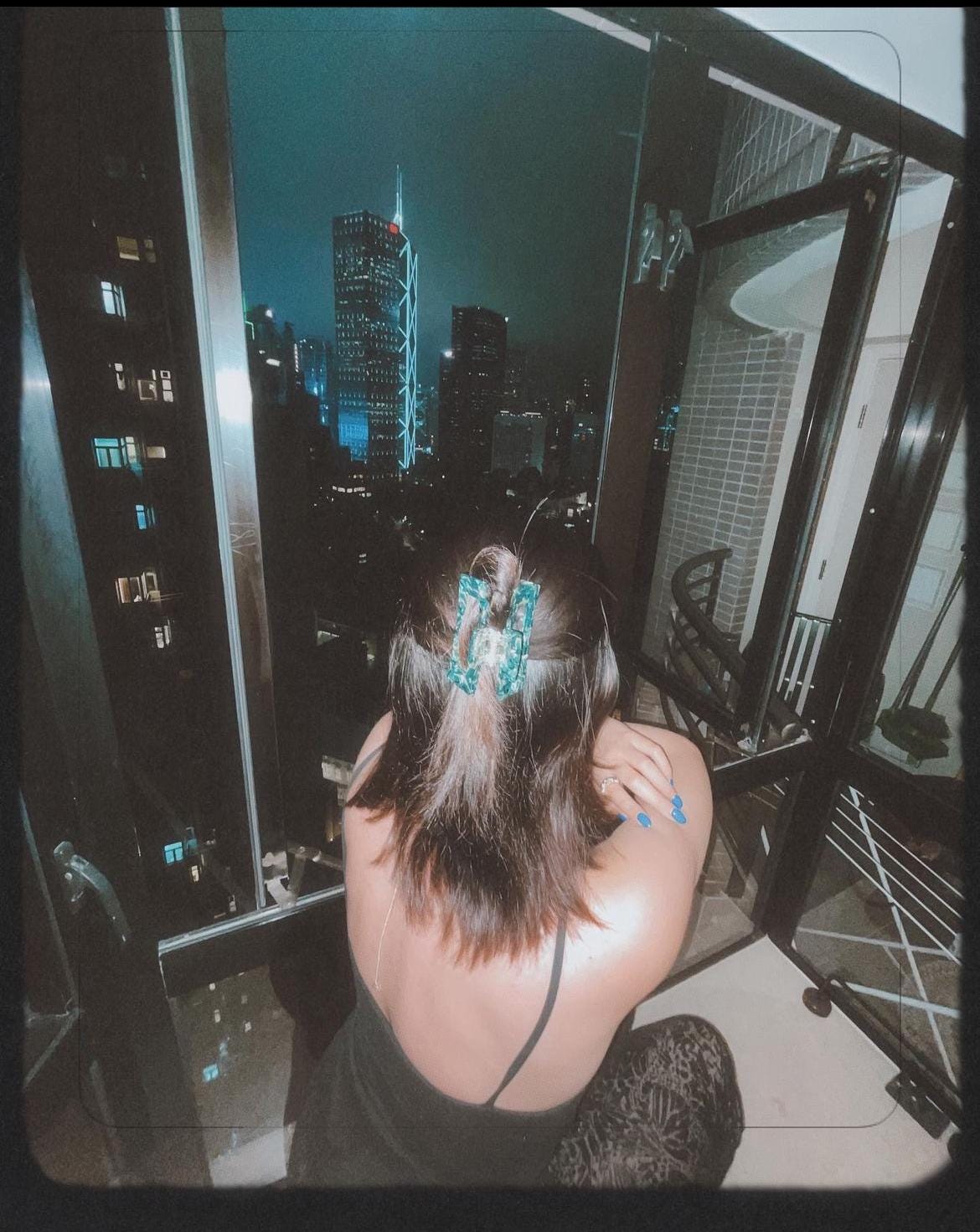 A woman from the back, looking out her window into a nighttime cityscape