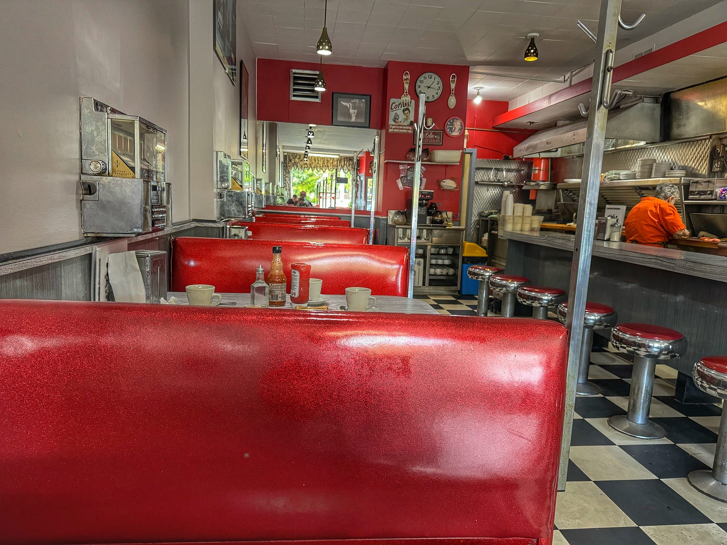 The interior of the Downsview Restaurant, as seen from one of the red sparkly booths along one wall. In the background, Betty the server is helping to prepare food.