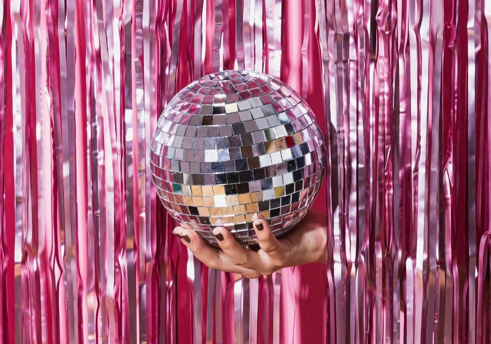 Girl holding disco ball with one hand through shiny pink tinsel curtain