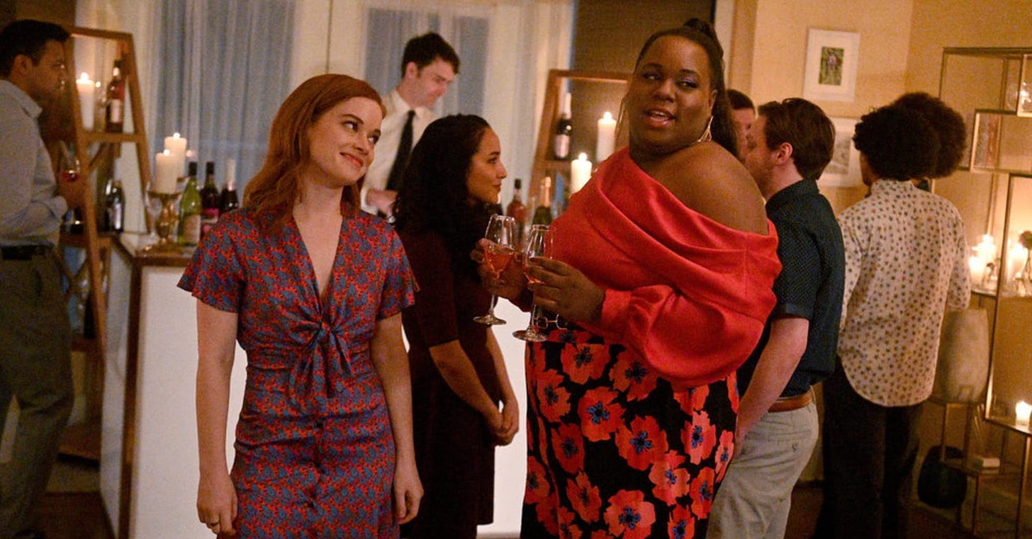 In a fancy houseparty scene, a ginger white woman looks adoringly at a genderqueer Black person who is holding two wine glasses while singing and looking adoringly at someone off camera.