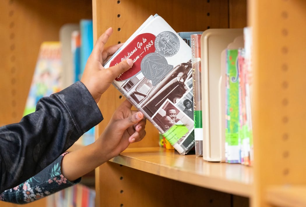 A detached hand reaches for a book on a shelf full of literature