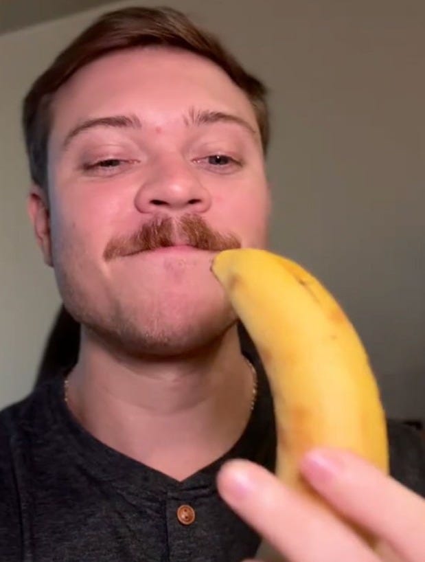 A man with a mustache holding a banana, potentially facing a fine for accidentally bringing a common item from overseas