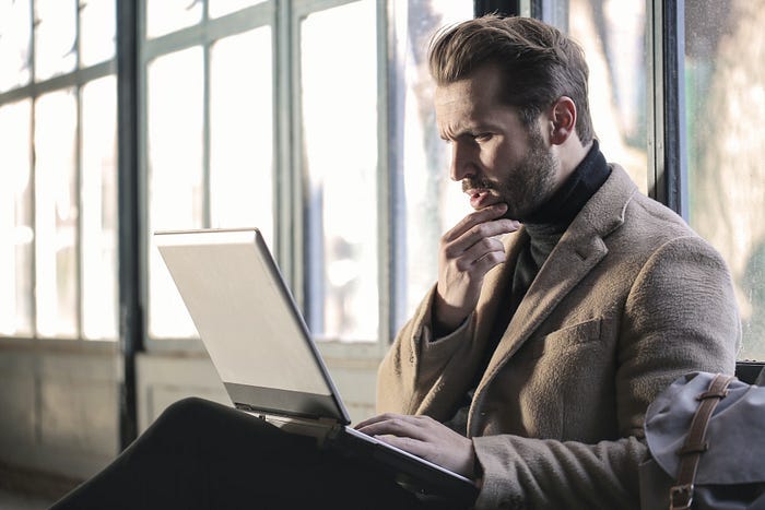 A confused-looking man staring at a laptop. A confused-looking man staring at a laptop.