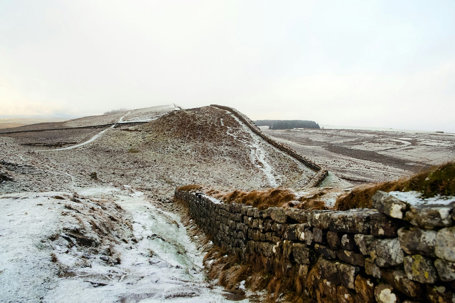 Snow-dusted Hadrian's Wall stretching across a rugged, rolling landscape in the United Kingdom, highlighting the historic Roman fortification built to mark the northern frontier of the Roman Empire.