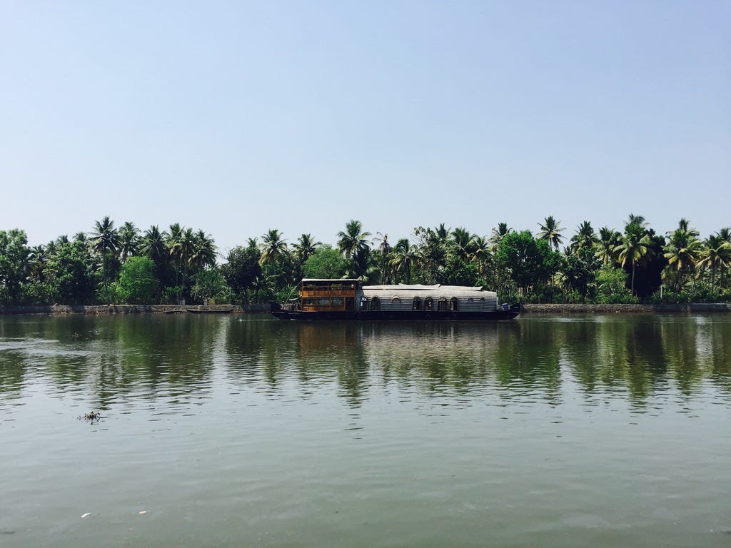 The first photograph I believe is from 2011 and  is of a Kettuvallam which is a houseboat widely used in the state of Kerala in India. These have thatched roof covers over wooden hulls. It is in the backwaters and behind the boat is a lush green canopy.