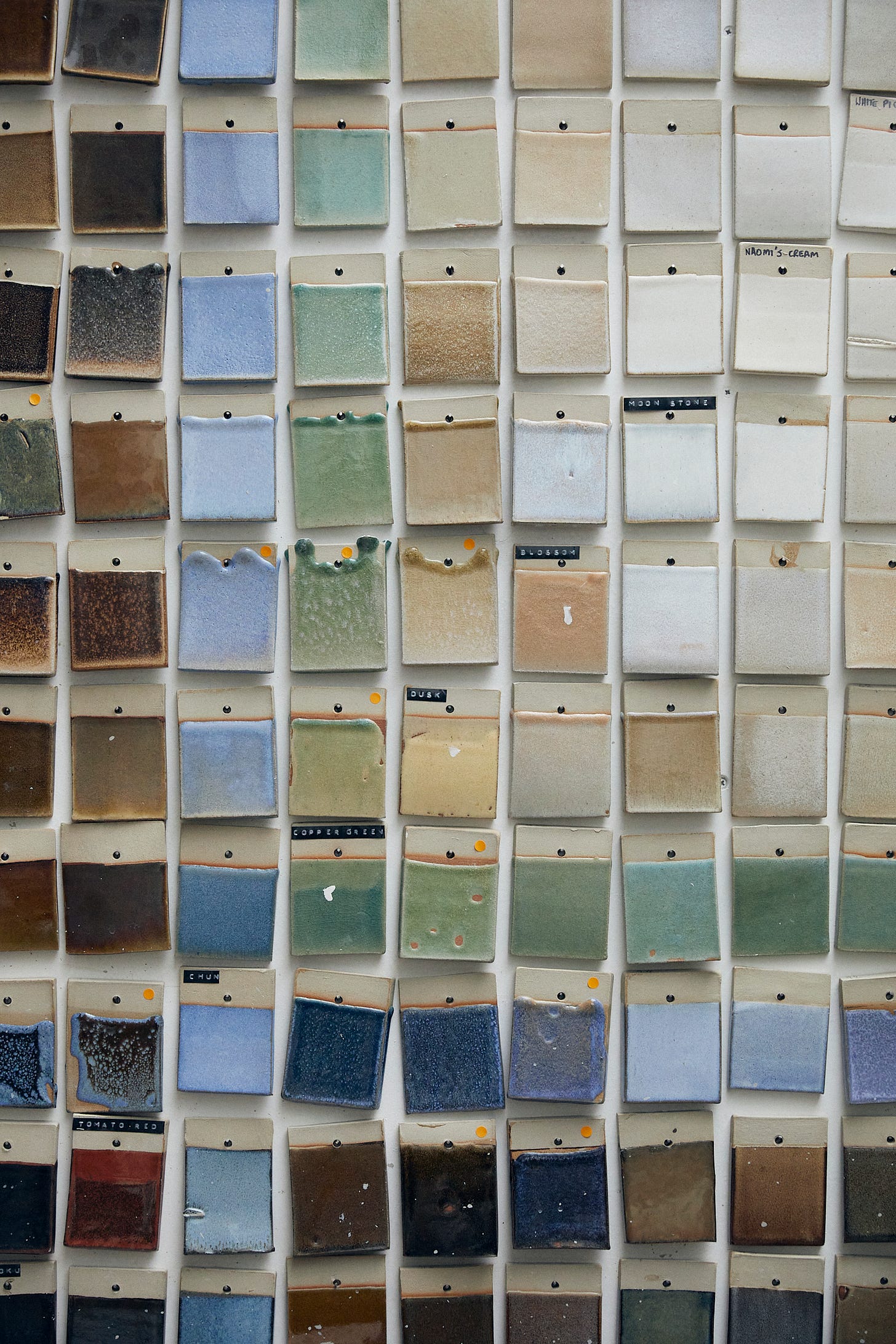 Ceramic rectangles pinned to a wall. They are glaze tests in a variety of earth colours.