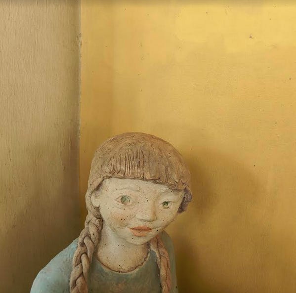A clay doll with yellow hair against a yellow wall.