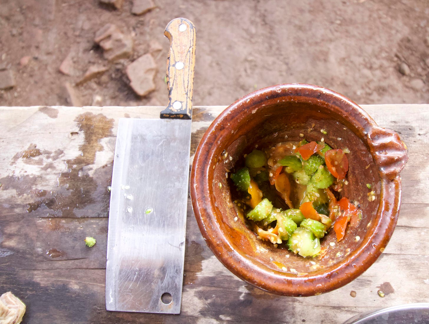 Image of pounded vegetables in a deep earthernware bowl with a big meat knife next to it