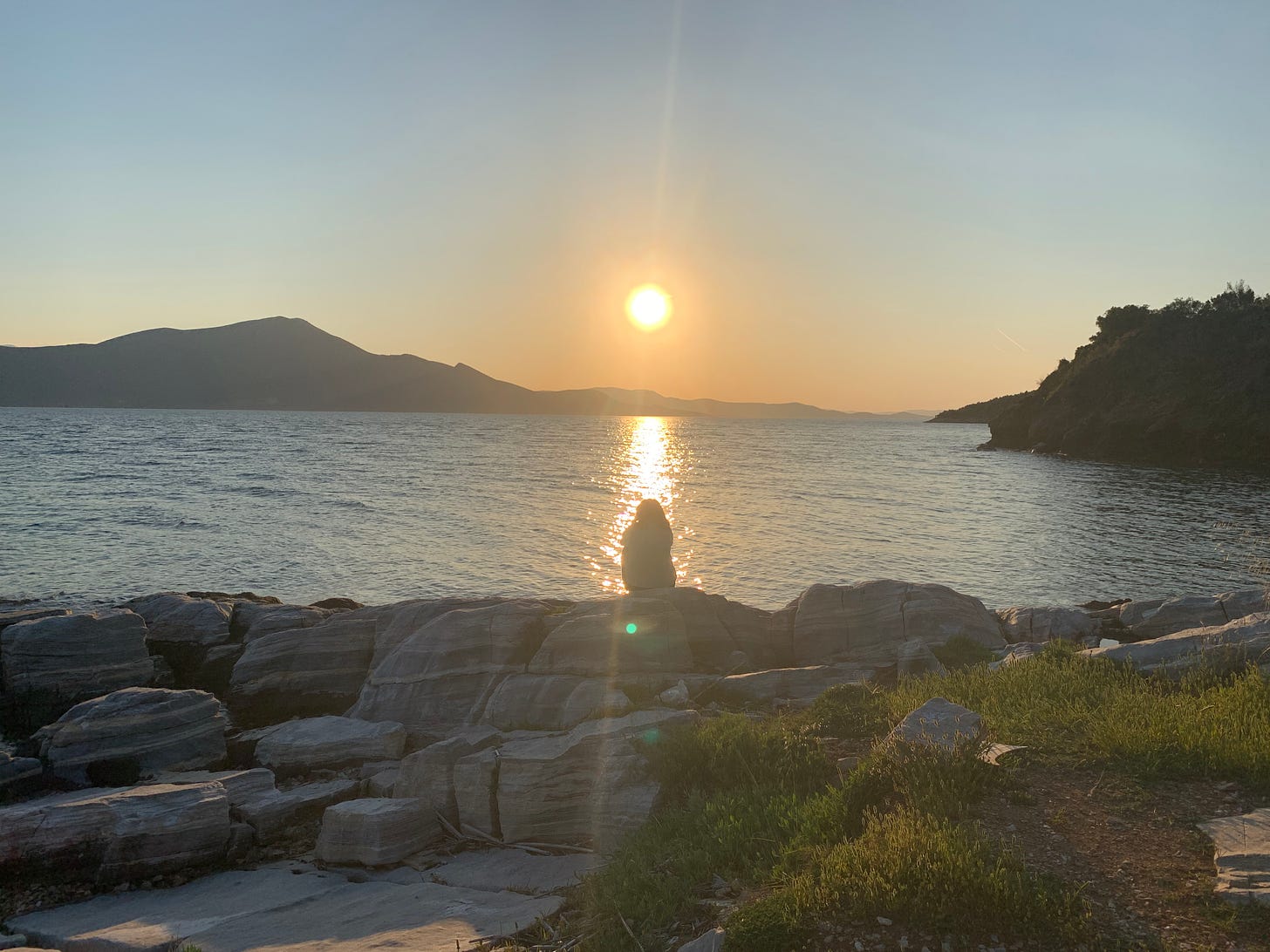 Woman sat on rocks watching the sun set over the sea