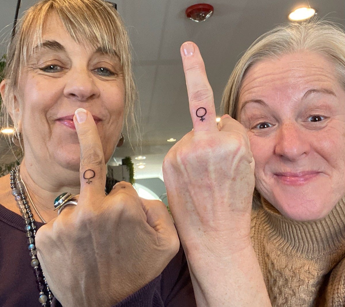 Two women with Venus symbol tattoos on their middle fingers