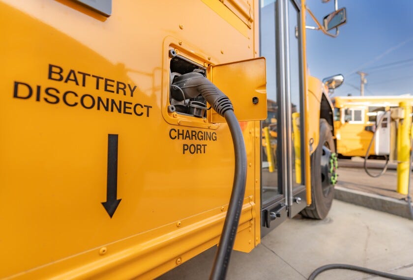 A close up photograph of an electric school bus charging at a charging station.