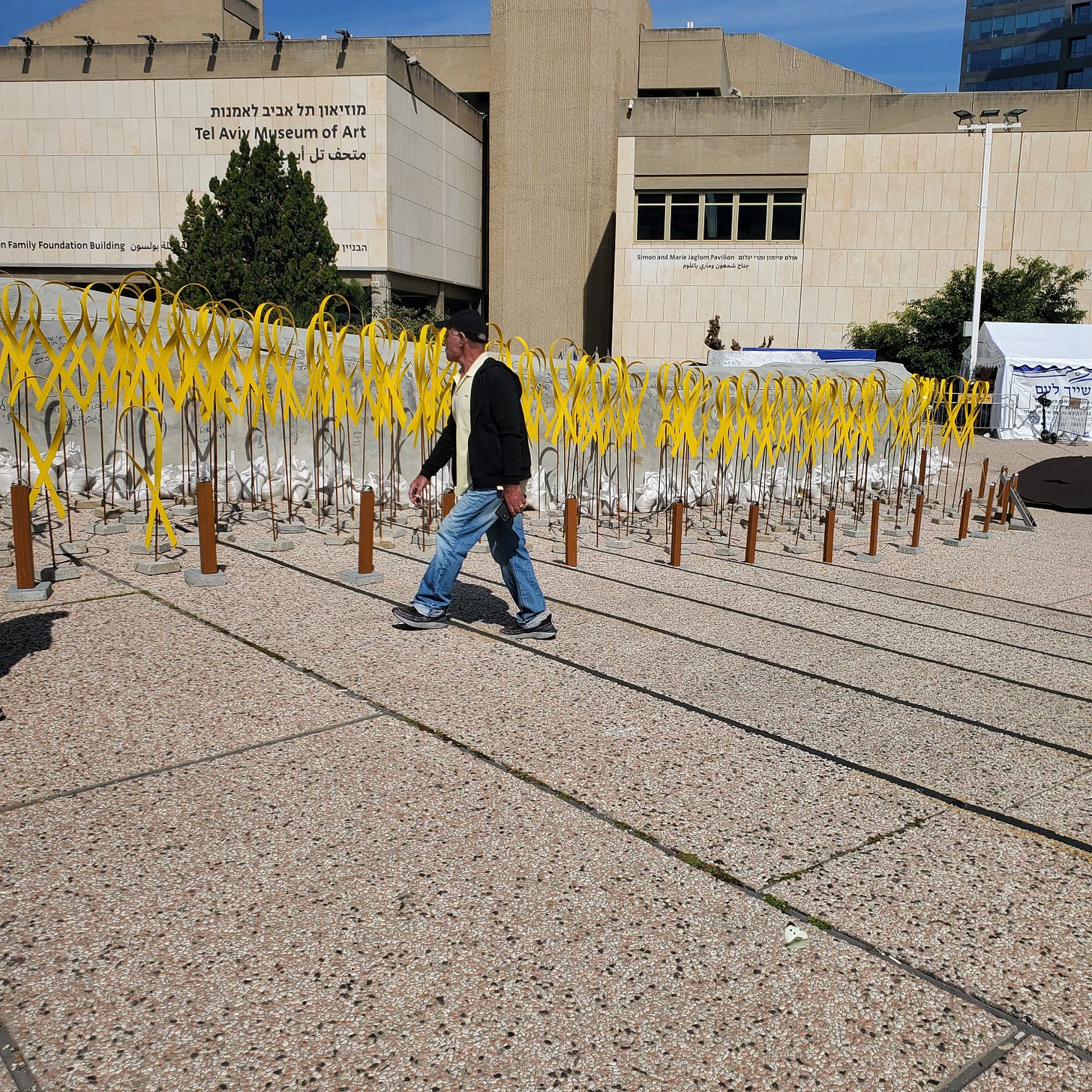 A man walks by a row of large metal yellow ribbons in front of the Tel Aviv Art Museum.