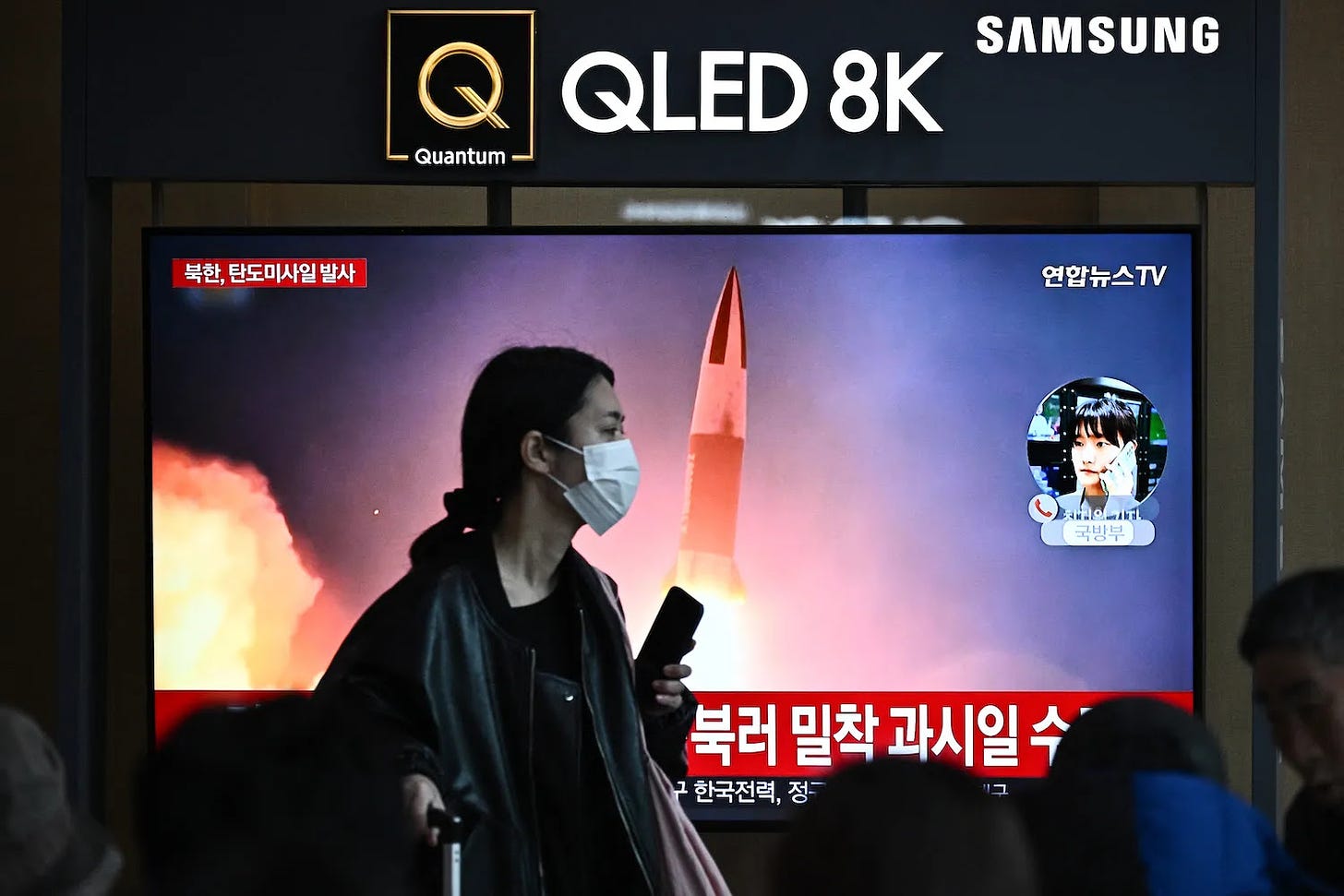 A woman walks past a television showing a North Korean missile test.