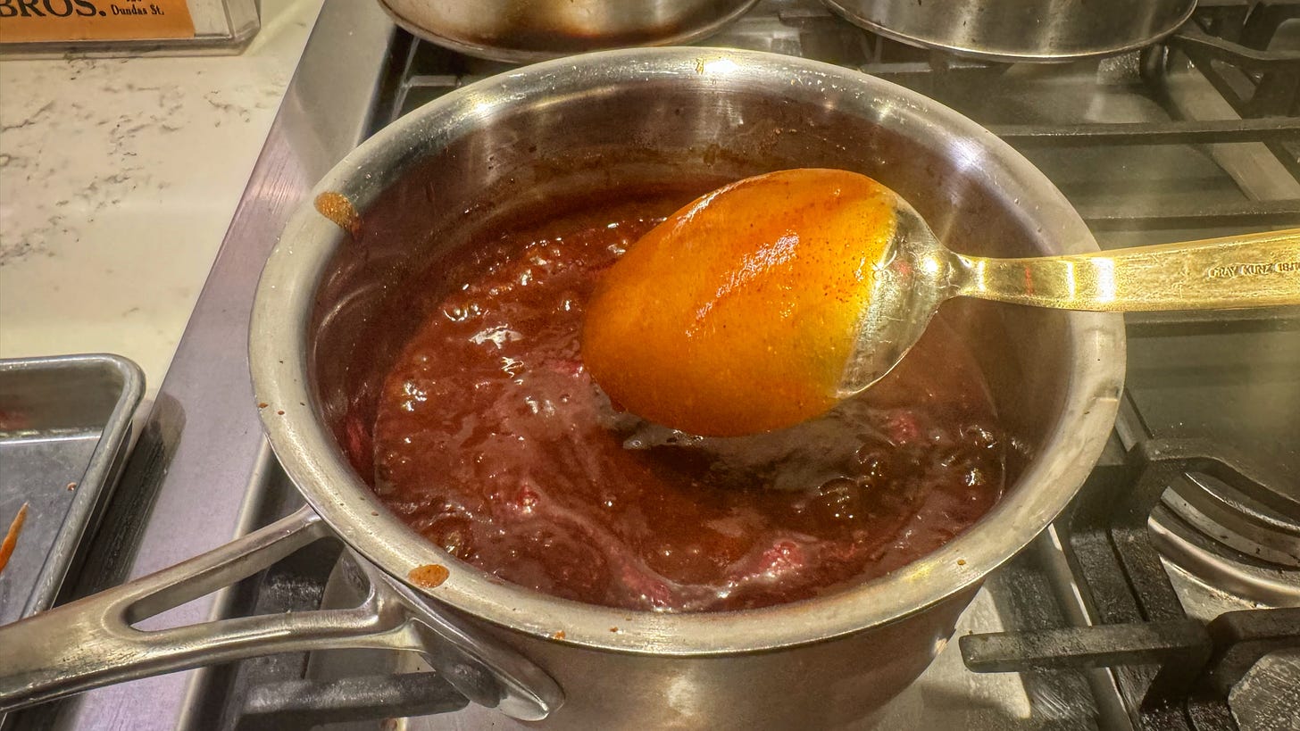 A saucepan full of mumbo sauce. A spoon held over the mumbo sauce shows the sauce is thick enough to coat it. 