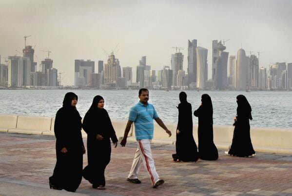 FILE- Qatari women and a man walk in front of the city skyline in Doha, Qatar, Saturday, April 7, 2012. The foreign fans descending on Doha for the 2022 FIFA World Cup will find a country where women work, hold public office and cruise in their supercars along the city's palm-lined corniche. (AP Photo/Kamran Jebreili, File)