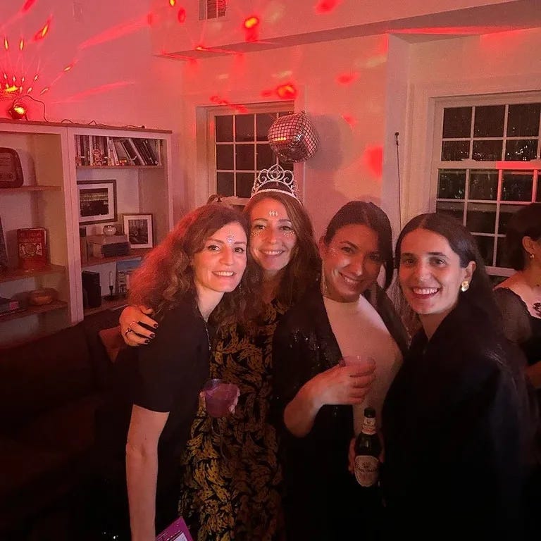 Four smiling women hug as they celebrate at a party.