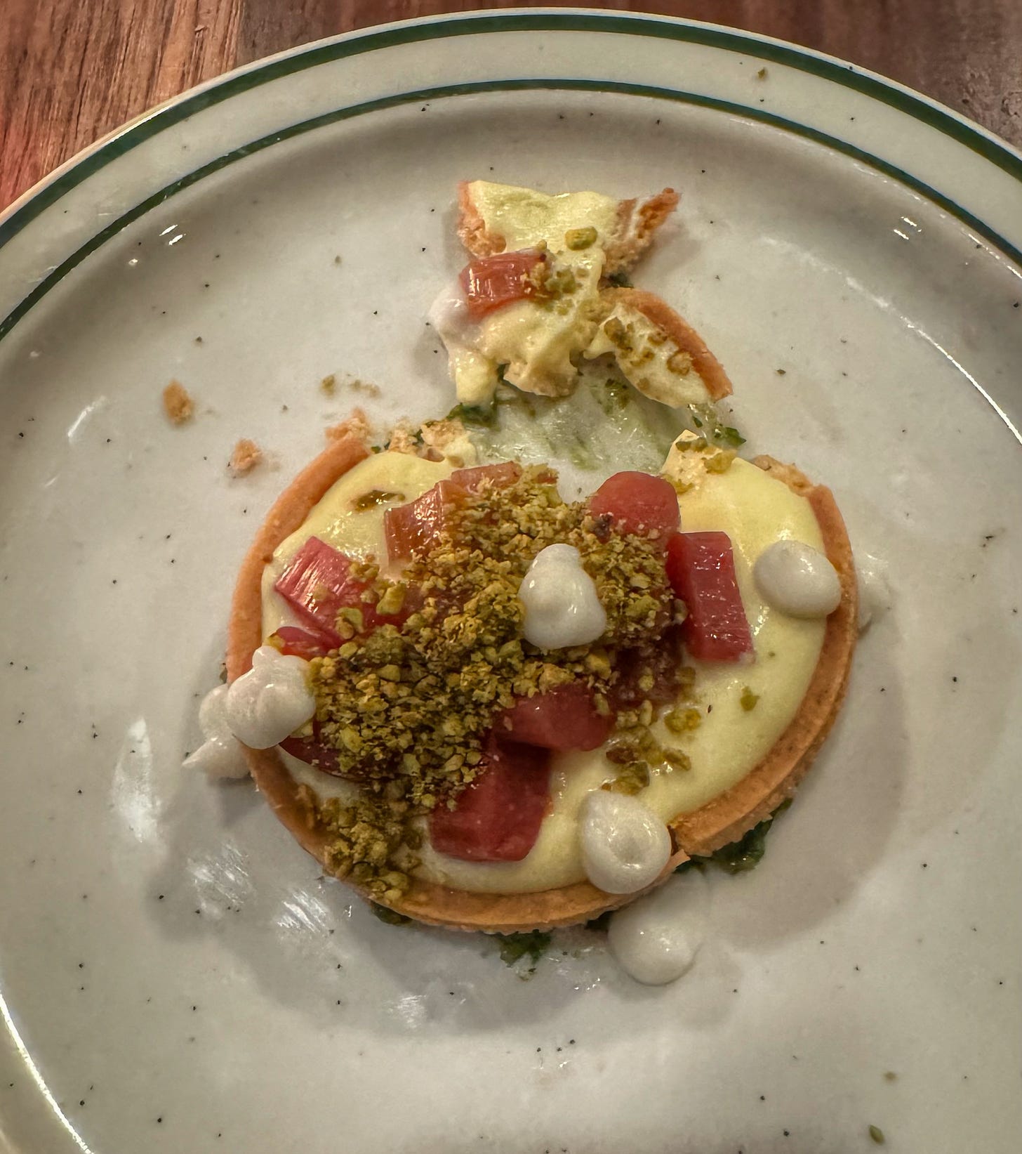 A tart consisting of a shortbread biscutit covered in a creamy zabaione sauce and topped with rhubarb and crushed pistachios