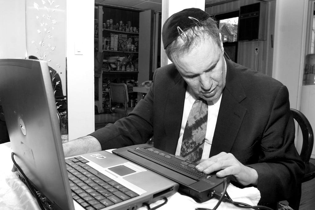 Rabbi Michael Levy works at his computer. He wars a kippah on his head, and is wearing a sportscoat, shirt and tie.